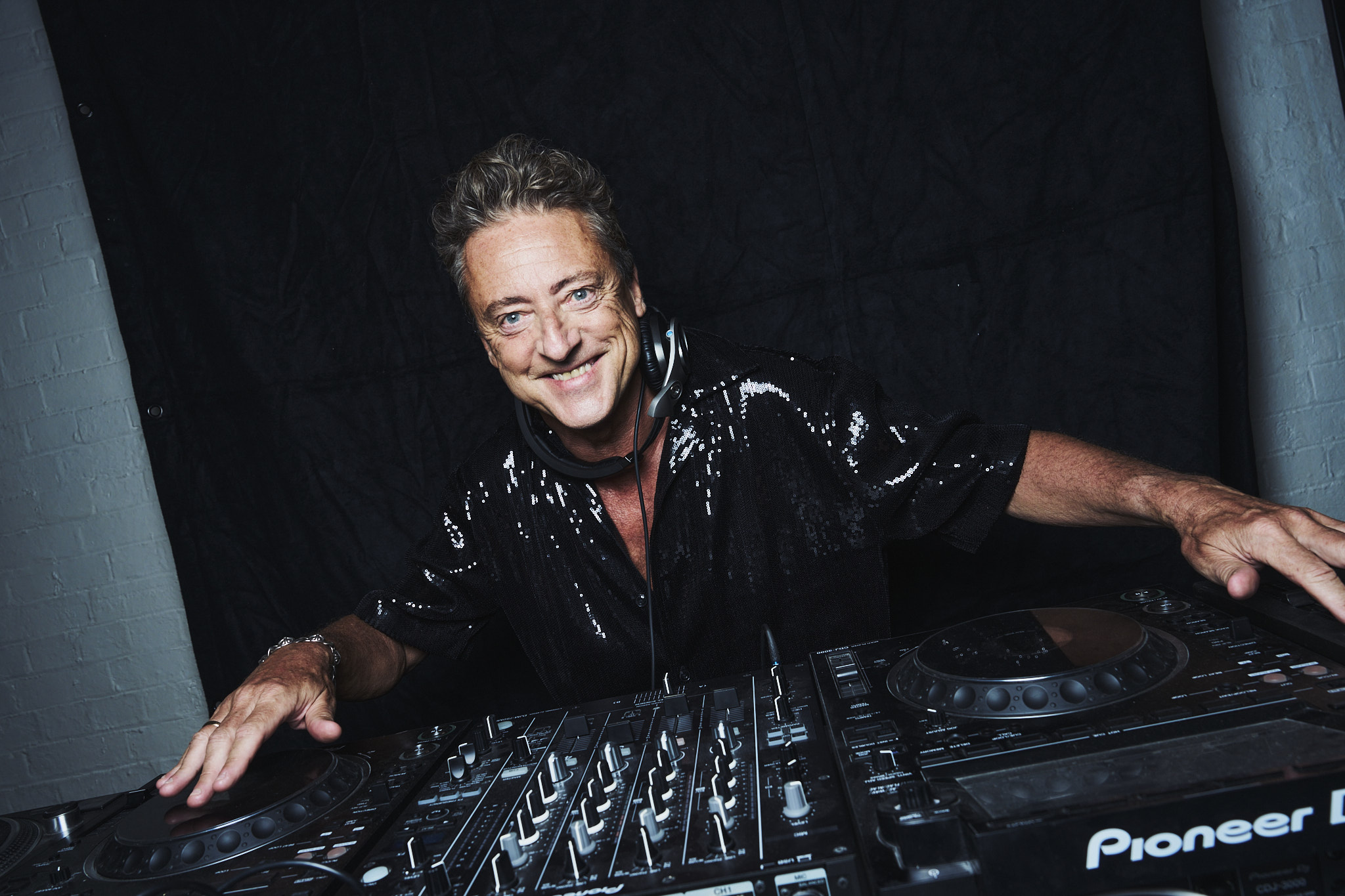 Jeremy Healy smiling behind the decks in a sequinned shirt