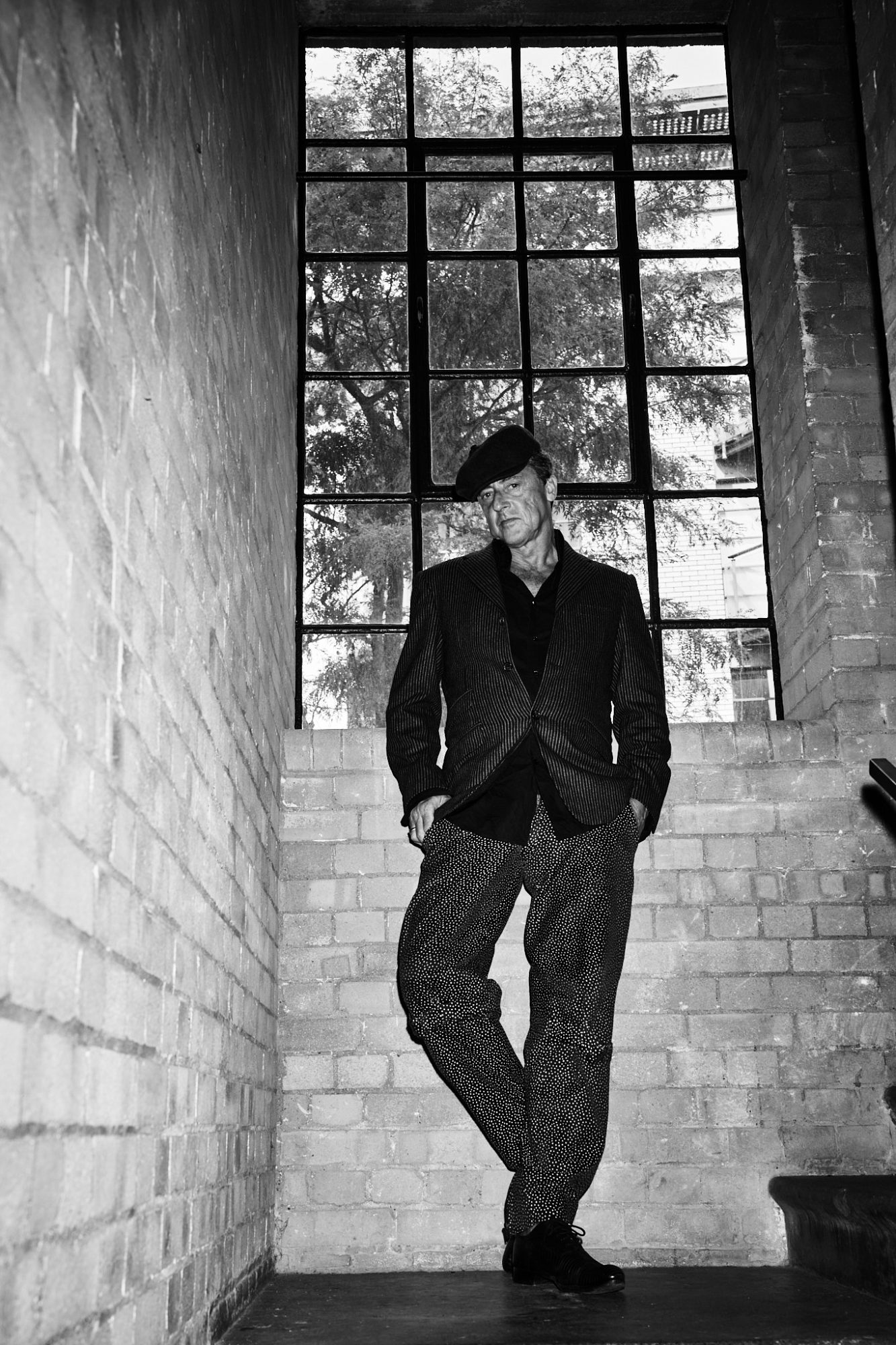 Jeremy Healy in a beret and pinstripe blazer, full length, brick stairwell